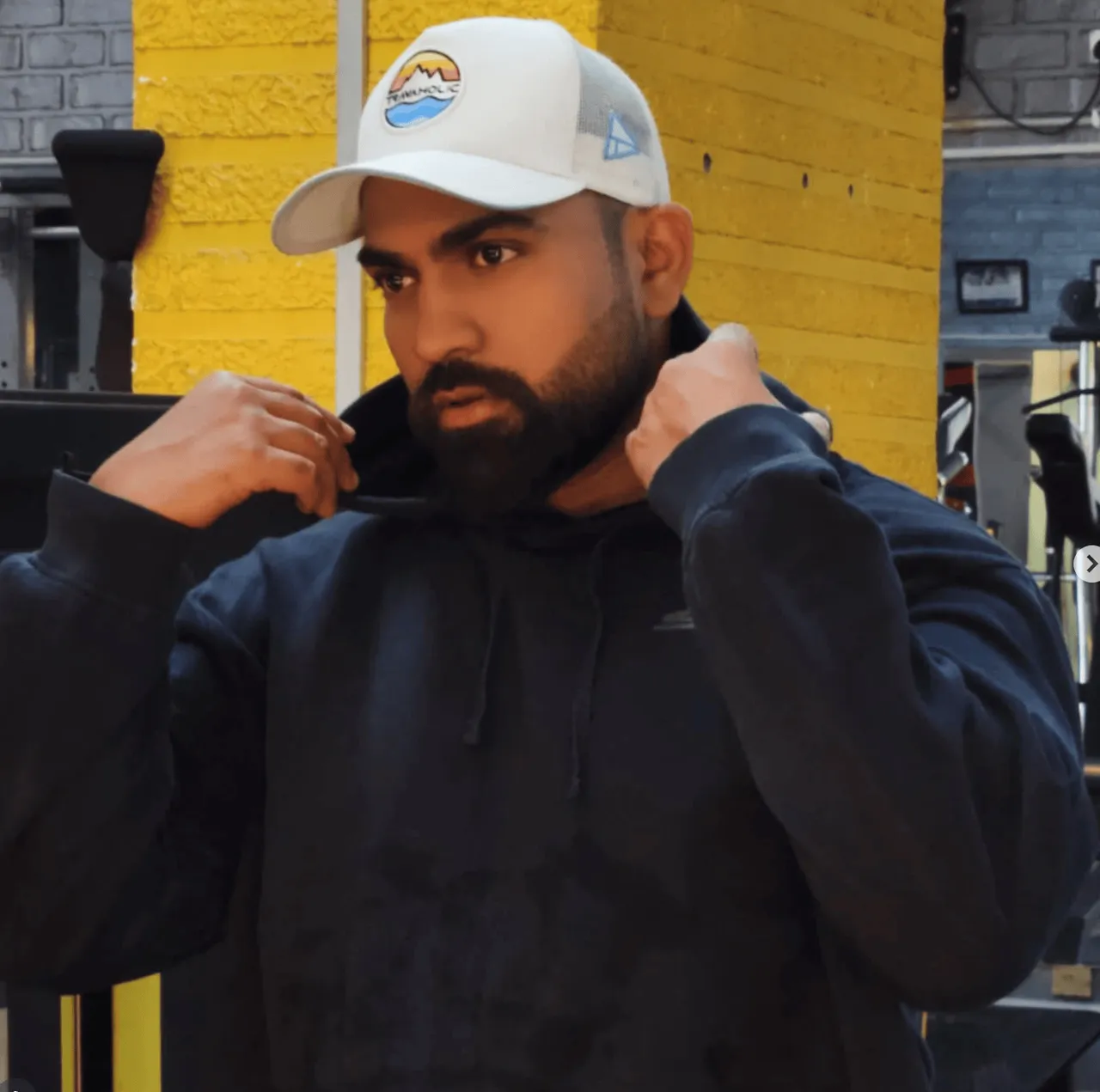 Golden hour on a city block, halfway through pulling a hoodie on — the cap doesn't come off either way.